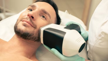 Young bearded man going through the procedure of skin analysis with a help of a modern device near his face
