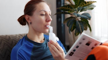 Caucasian woman is reading book and holding nebulizer tube inhaling vapors of medicines into her lungs