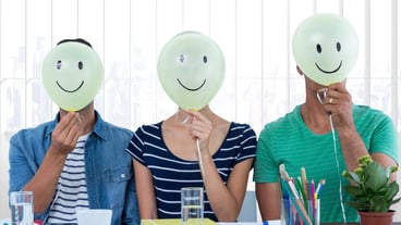 Colleagues holding smiley while sitting on desk