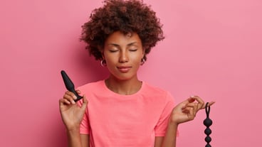 Pleased woman poses with anal beads, butt plug used to enchance climax, for pleasurable feelings in anus, achieves sexual pleasure with help of sex toys. Erotic stimulation focused on anus and rectum
