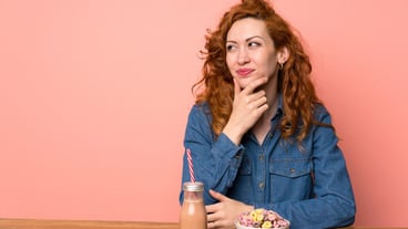 Redhead woman having breakfast cereals and fruit thinking an idea