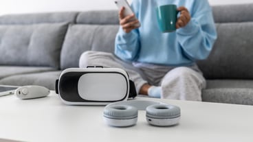 Woman on sofa holding her phone and a mug, sitting in front of a table of gadgets