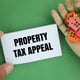 in hand there is a house form and paper with the word Property Tax Appeal