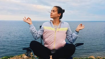 Young woman meditating while sitting on a chair at the beach against a cloudy sky