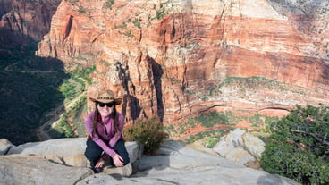 High angle portrait of a woman perched on a cliff against Zion Canyon