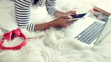 Midsection of woman using laptop and mobile phone on bed at home