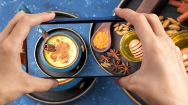 Female hands holding a smartphone above a blue cup of Ayurvedic drink golden turmeric milk latte