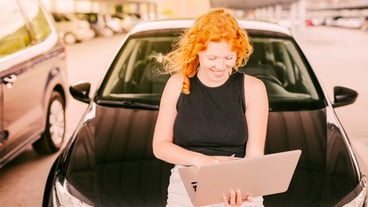 Woman with laptop sitting on hood of car