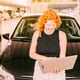 Woman with laptop sitting on hood of car