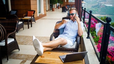 Freelancer concept. Successful young man, businessman working on a laptop computer, sitting on the terrace drinking coffee and talking on the phone.