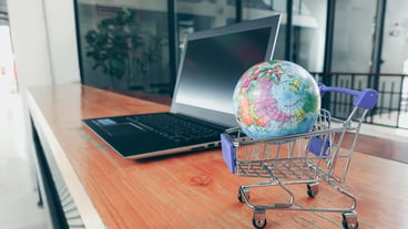 Close-up of globe in shopping cart by laptop on table