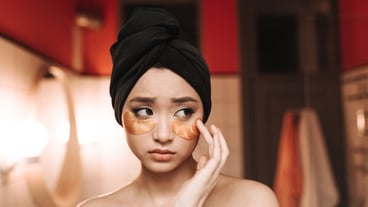 Lady in towel puts on patches to moisturize skin under eyes