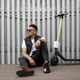 Stylish nice young hipster man in dark sunglasses in trendy summer clothes resting after riding an electric scooter