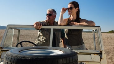 Couple looking away while standing in vehicle on field