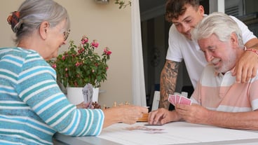 Happy multi generation family enjoying free time together sitting outdoors smiling playing cards