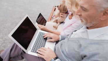 A woman has a dog, a man is holding a laptop on his lap.