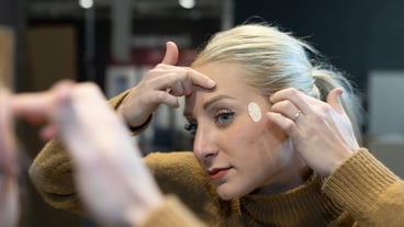 Young woman applying acne patch in front of mirror