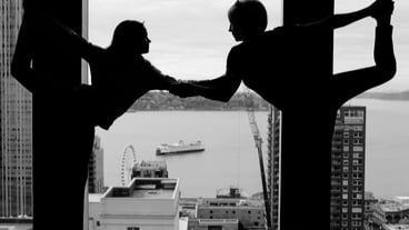 Silhouette man and woman practicing yoga against glass window