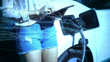 Blue wave design vs. woman using digital tablet while charging electric car at charging station