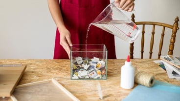 Woman pouring water in container filled with paper pieces at workshop