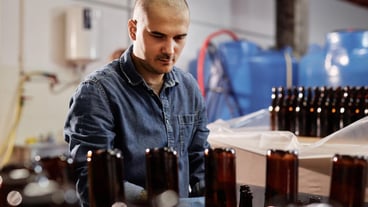 Hard Working Male Production Operator Standing at Conveyor in Workshop of Cider or Beer Plant