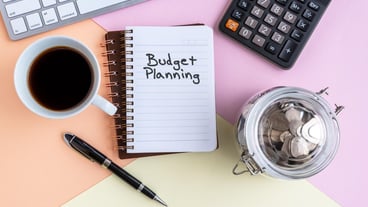 Budget Planning text on note pad with cup of coffee calculator computer keyboard coin jar and pen