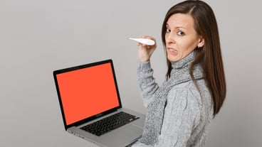 Side view of confused woman with sweater and scarf holding thermometer and laptop with blank screen, isolated on gray background. Concept for healthy lifestyle and online treatment during the cold season.
