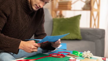 Young man making greeting card for New Year and Christmas 2021 for friends or family, scrap booking, DIY. Writing a letter with best wishes, design his homemade card. Holidays, celebration.