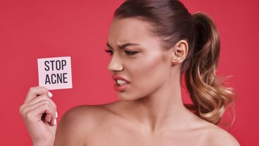 Skin problems.  Young woman holding a small porter and making a face while standing against pink background