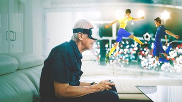 An elderly man plays a game of football with virtual reality glasses.