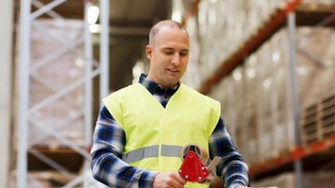 Logistik, Lieferung, Versand, Menschen und Exportkonzept - glücklicher Mann in Sicherheitsweste Verpackungskiste oder Paket mit Klebeband im Lager oder Postlager