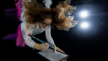 A smiling young mermaid writing while swimming underwater