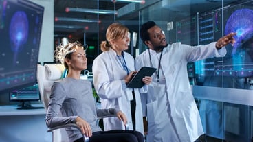 Woman Wearing Brainwave Scanning Headset Sits in a Chair while Two Scientists Supervise and Look at Data In the Modern Brain Study Laboratory Monitors Show EEG Reading and Brain Model