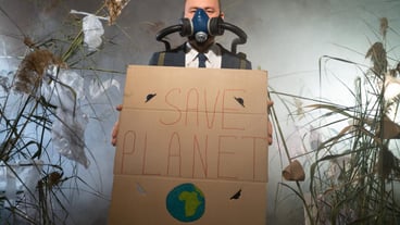 A man with a gas mask in a suit shrouded in smoke walks through a dangerous radioactive zone with a Save Planet poster Plastic disaster Environmental disaster