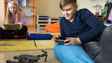 Young boy trying out a drone while young girl is working using a tablet