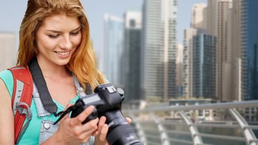 adventure, travel, tourism, hike and people concept - happy young woman with backpack and camera photographing over dubai city waterfront background