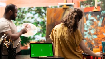 Diverse artists painting on canvas next to green screen display