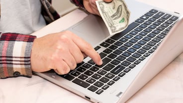 A person is holding a dollar bill front their laptop a pushing Enter with buyer online concept