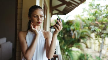 A young beautiful woman looks at her face with makeup in the mirror outside in the summer protective spf products for problem skin with acne