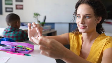 Smiling caucasian young female teacher teaching through sign language in classroom