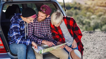 Young friends travelers sitting on trunk of car and looking at the paper map.