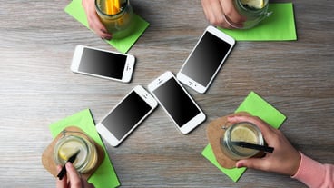 Four hands with smart phones holding cocktails on wooden table background