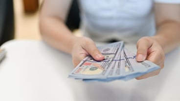 책상에 앉아 있는 아시아 여성이 100달러 지폐 뭉치를 들고 자른 이미지