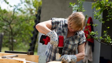 Senior caucasian woman assembles a wooden frame of building using metal fasteners using screwdriver
