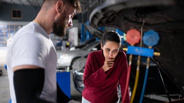 A car mechanic working in a car repair shop explains to the customer