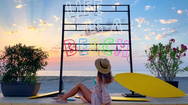 Fashionable young woman on the beach sitting under a colorful neon sign