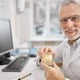 Cheerful elderly dentist holding a full jaw dental implant while smiling at the camera