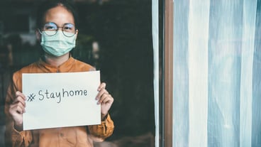 Asian girl wearing glasses, wearing a mask, holding paper labeled #stayhome, is bored of having to detain and treat the illness at home alone. Concept home quarantine, prevention COVID-19