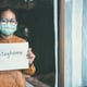 Asian girl wearing glasses, wearing a mask, holding paper labeled #stayhome, is bored of having to detain and treat the illness at home alone. Concept home quarantine, prevention COVID-19