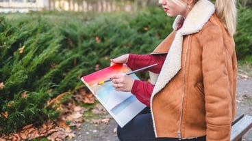 Portrait of a young artist girl who sits on a bench and draws a picture